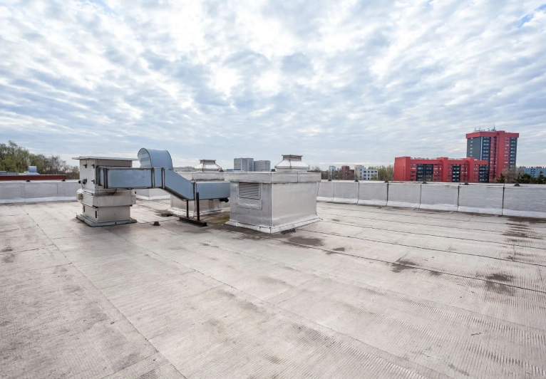 A rooftop view featuring metallic ventilation systems against a backdrop of cloudy skies and urban buildings.